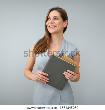 Smiling business woman wearing grey dress, holding work books and looking away. Isolated female portrait. 