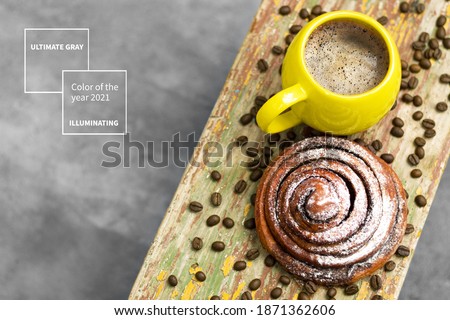 A mug of coffee with a sweetest kanelbulle demonstrating trendy illuminating yellow and ultimate gray colors of the year 2021. Design for color illustration.