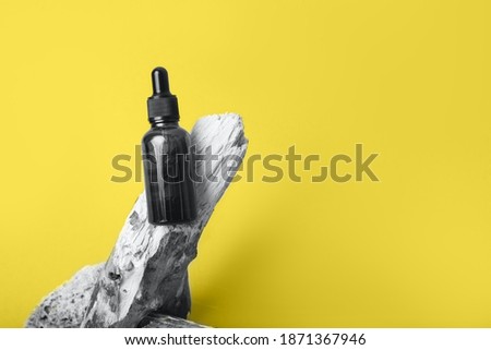 A glass dropper bottle with a pippette with black rubber tip on the tree branch on the yellow background. Nature Skin concept. Organic Spa Cosmetics. Trendy concept. Demonstrating Color 2021. Yellow