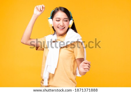 Young woman listening favorite music by headphone and dancing over yellow background. Happy relaxed young female in headphones dancing and listening to music. Women over isolated yellow background.
