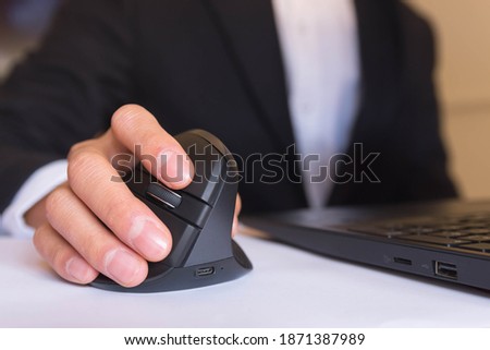 A person working at home in front of a computer holding a computer ergonomic mouse. Royalty-Free Stock Photo #1871387989