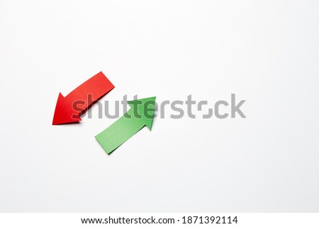 Two opposite direction right-up left-down arrows, cutted from the red and green paper on the white plain paper background