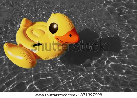 Bright yellow inflatable swimming duck in ripple water in swimming pool of resort hotel with sun reflection. Summer holiday concept, background with copy space. Trendy colors of 2021 year.