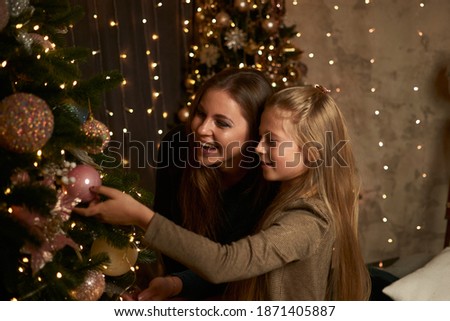Happy mom and daughter decorate the Christmas tree on the background of garlands. Family, new year, christmas.