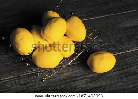 Iron stand with fresh lemons on an old vintage wooden table. Retro rustic view. Trendy color of 2021 year.
