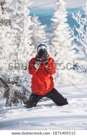 Photo of woman in fur coatski outfit sitting in snowy trees closing, her eyes over white snow in magic winter day. Woman take snow in her hands and throw it to her own face. Snow