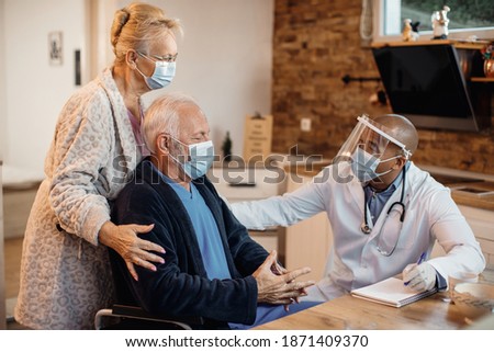 Mature couple and black doctor wearing protective face masks while talking at nursing home. Royalty-Free Stock Photo #1871409370