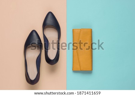 Minimalistic fashion still life. Classic women’s high heel shoes, yellow leather wallet on pink blue pastel background.