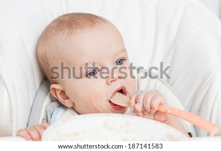 cute baby boy eating on her own with big spoon on a white background
