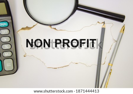 the word non profitwritten on a white sheet of paper which lies on the table and on a white background, next to a magnifying glass pens calculator. High quality photo