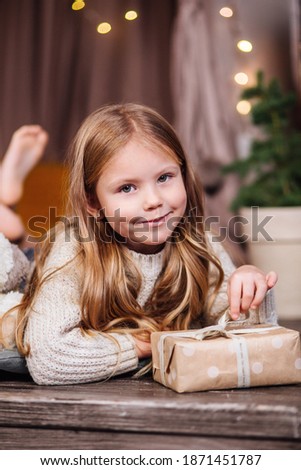 Happy curly little child girl lying and opening gift on the background with lights. Merry Christmas