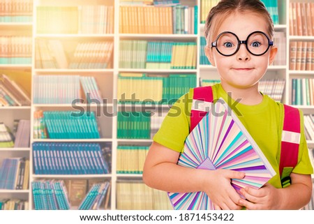 Little girl with school backpack and notebook stands in the library. High quality photo