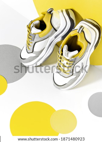 Bright scene with casual chunky sneakers and huge confetti in main colour of the year 2021.  Illuminating and ultimate gray minimalist background. Sport and fitness idea.
