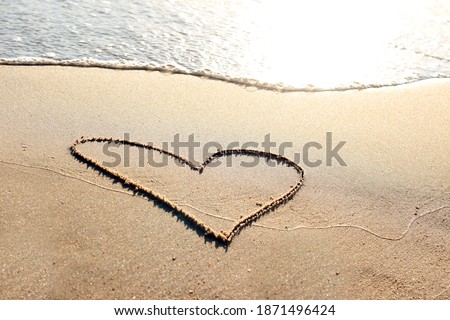 Heart drawn on the sand by the sea, a romantic symbol for Valentine's Day, top view, a coast of yellow sand with a light blue wave.
