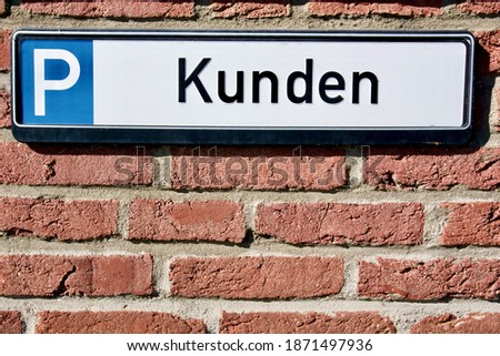 A closeup of a parking nameplate with the writing "Kunden - Customers" on a red brick wall