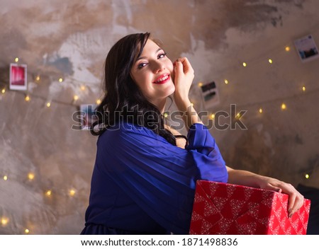 A young woman holds a gift near the Christmas decoration. The girl smiles sitting on a bed with a gift for Christmas