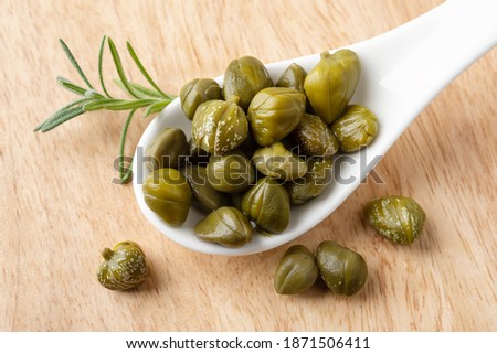 Pickled capers in a white porcelain spoon on a brown wooden cutting board. Marinated buds of caper bush. Mediterranean cuisine ingredient. Organic spices and seasonings. Top view. Royalty-Free Stock Photo #1871506411