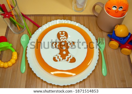 Children's table setting. Three children's plates on a wooden napkin with a plastic spoon and fork, a Cup, tubes and bright toys. Gingerbread man as a symbol of Christmas. The first solid foods.