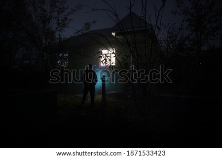 Old house with a Ghost in the forest at night. Horror silhouette at the window. Horror Halloween concept Alone man silhouette standing near window of house at night. Selective focus