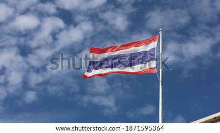 Thai flag on top flagstaff. The Thai national flag is waving in beautiful waves with the wind. On the blue sky background there are thin white clouds. selective focus