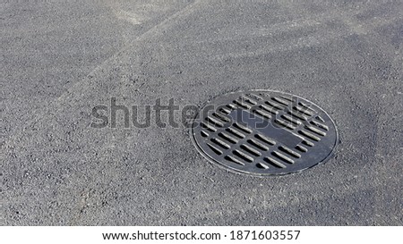 Manhole round metal grate on roadway.Steel grating filters the debris of drains and pits on the pavement to prevent urban flooding. On an asphalt road background with copy space. Selective focus