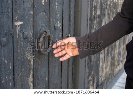 A closeup shot of a man's hand trying to open an old vintage door with a round iron handle
