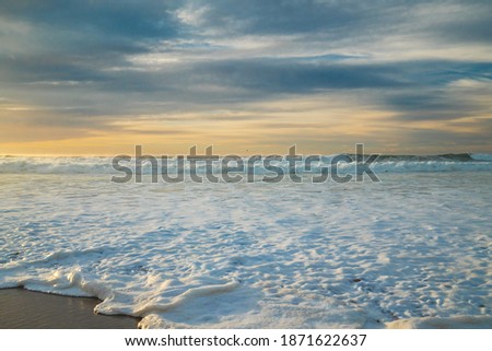 Sunset over the sea. Stormy waves and sea foam on the beach with beautiful cloudy sky on background