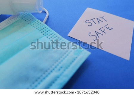 A shot of a medical mask, sanitizer, and a card with "stay safe" text on a blue background
