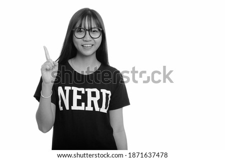 Young happy Asian nerd teenage girl smiling and pointing finger up