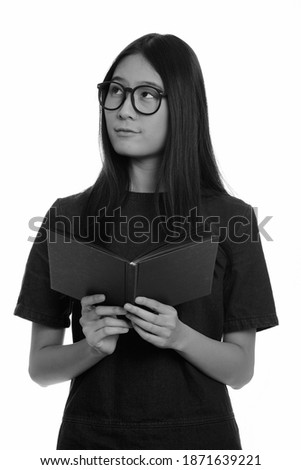 Young beautiful Asian teenage girl holding book while thinking