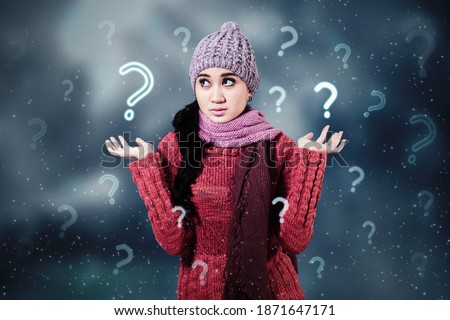Picture of young woman wearing winter clothes while looks confused and standing with question marks symbol background