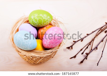 colored easter eggs in nest on rustic wooden planks with branch