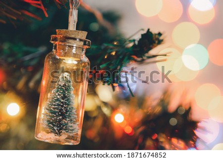 Christmas decoration. Hanging small Christmas tree in glass jar on pine branches Christmas tree garland and ornaments over abstract bokeh