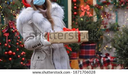 Safe delivery of gifts and packages for the holidays in quarantine during the coronavirus pandemic.Beautiful girl volunteer in a medical mask, gloves and santa hat a gives gift box.Copy space for text