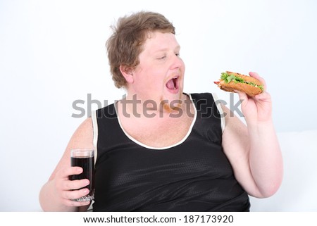 Fat man eating tasty sandwich and drink cola on home interior background  