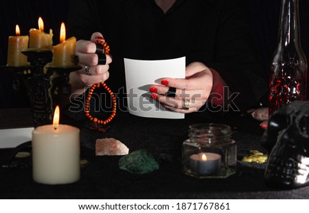 The fortune teller is holding a photo and a rosary. Fortune-teller's hands, candles, and skulls on a black table. The concept of wizards, witchcraft and magic.