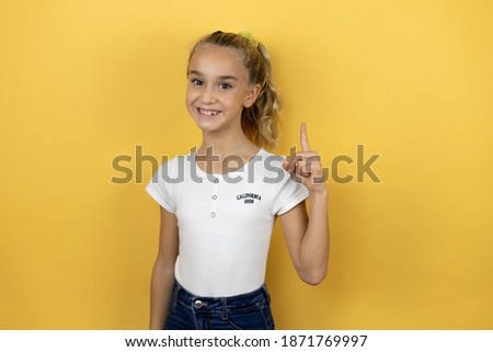 Young beautiful child girl standing over isolated yellow background showing and pointing up with fingers number one while smiling confident and happy
