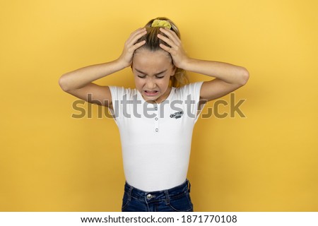 Young beautiful child girl standing over isolated yellow background suffering from headache desperate and stressed because pain and migraine with her hands on head