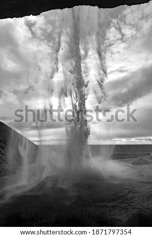 Seljalandsfoss magical Waterfall from cave behind in the south of the Iceland with water curtain and cloudy sky. Major Tourist attraction and natural wonder on coastal ring road, black and white
