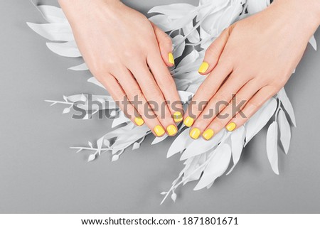 Woman hands with yellow manicure on the gray background. Trendy colors 2021 concept. Flatlay, top view. Copy space.