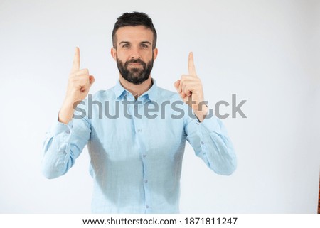 Young man wearing casual blue shirt pointing fingers up over white background.