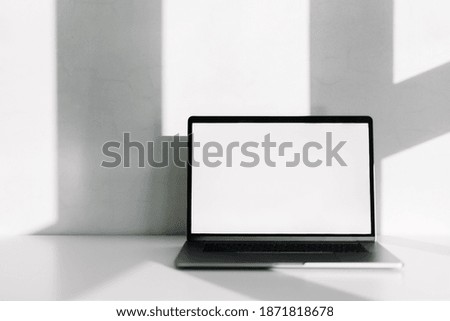 Laptop computer with white blank screen on the white table with shadow from window.