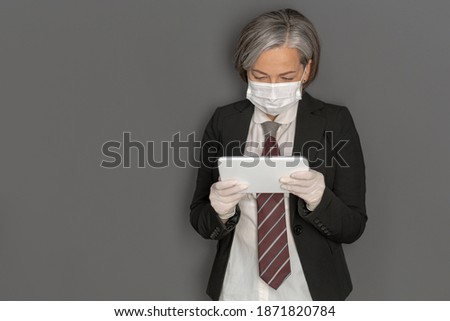 Caucasian businesswoman in protective mask work digital gadget isolated on grey background. Portrait of modern senior woman in studio wearing business clothes. 