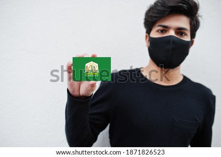Indonesian man wear all black with face mask hold Aceh flag in hand isolated on white background. Provinces of Indonesia coronavirus concept.