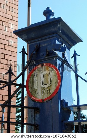 Close Up of Faded Circular Sign on Iron Gatepost of Old Industrial Building 