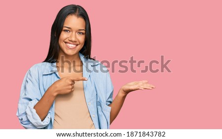 Beautiful hispanic woman expecting a baby showing pregnant belly amazed and smiling to the camera while presenting with hand and pointing with finger. 