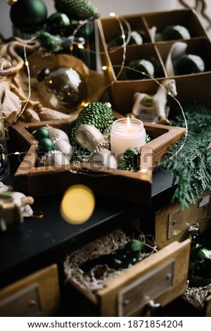 Christmas layout: green and silver coloured ornaments and baubles in stars, acorns and pine cones shapes, pine branch and a cute burning candle in the star shaped wooden tray, close up view