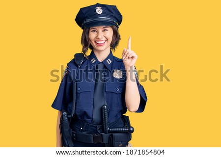 Young beautiful girl wearing police uniform showing and pointing up with finger number one while smiling confident and happy. 