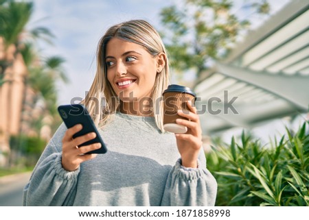 Young blonde girl using smartphone and drinking coffee at the city