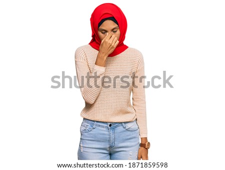 Young african american woman wearing traditional islamic hijab scarf tired rubbing nose and eyes feeling fatigue and headache. stress and frustration concept. 